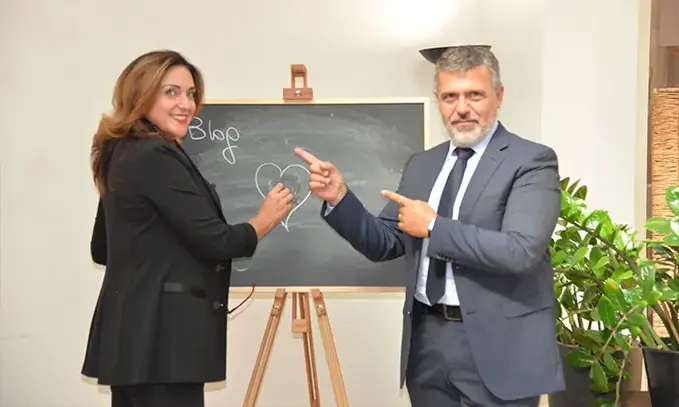Silvia Rossi e un suo collega indicano sorridendo una lavagna alle loro spalle.